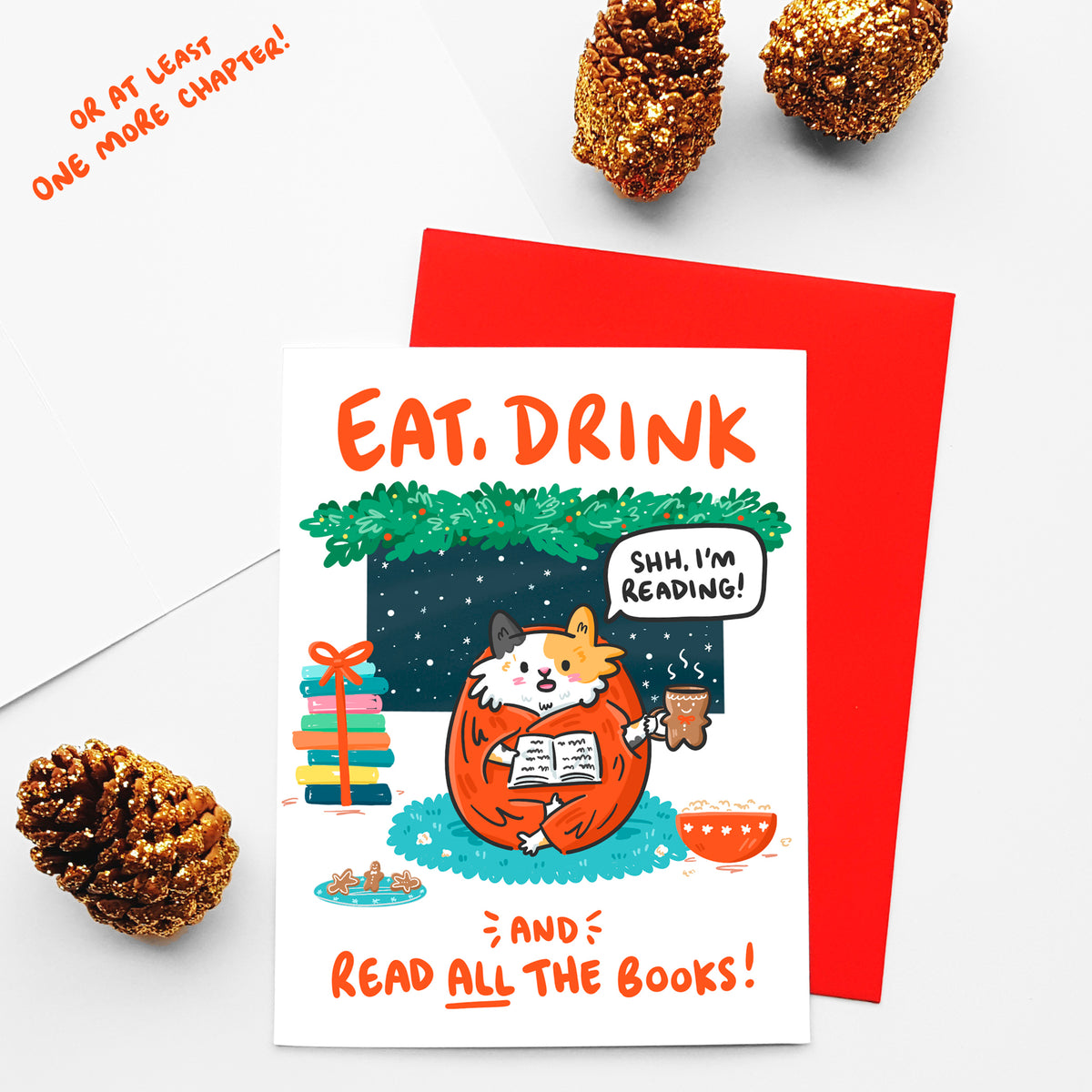 Holiday greeting card with calico cat reading a  book and drinking tea out of a gingerbread mug while it snows around Christmas